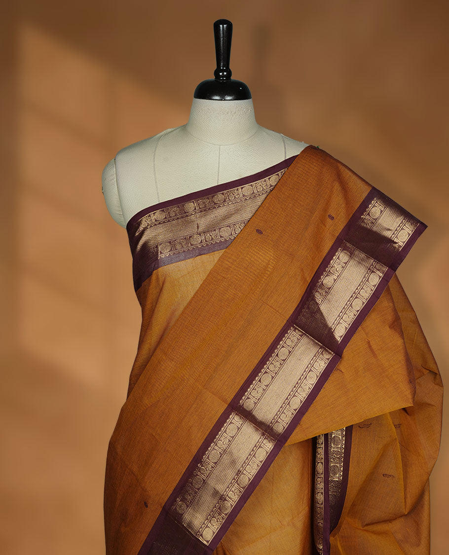 Mustard Brown colour chettinad cotton saree featuring plain body, paired with a black colour traditional gold zari border paired with matching blouse.