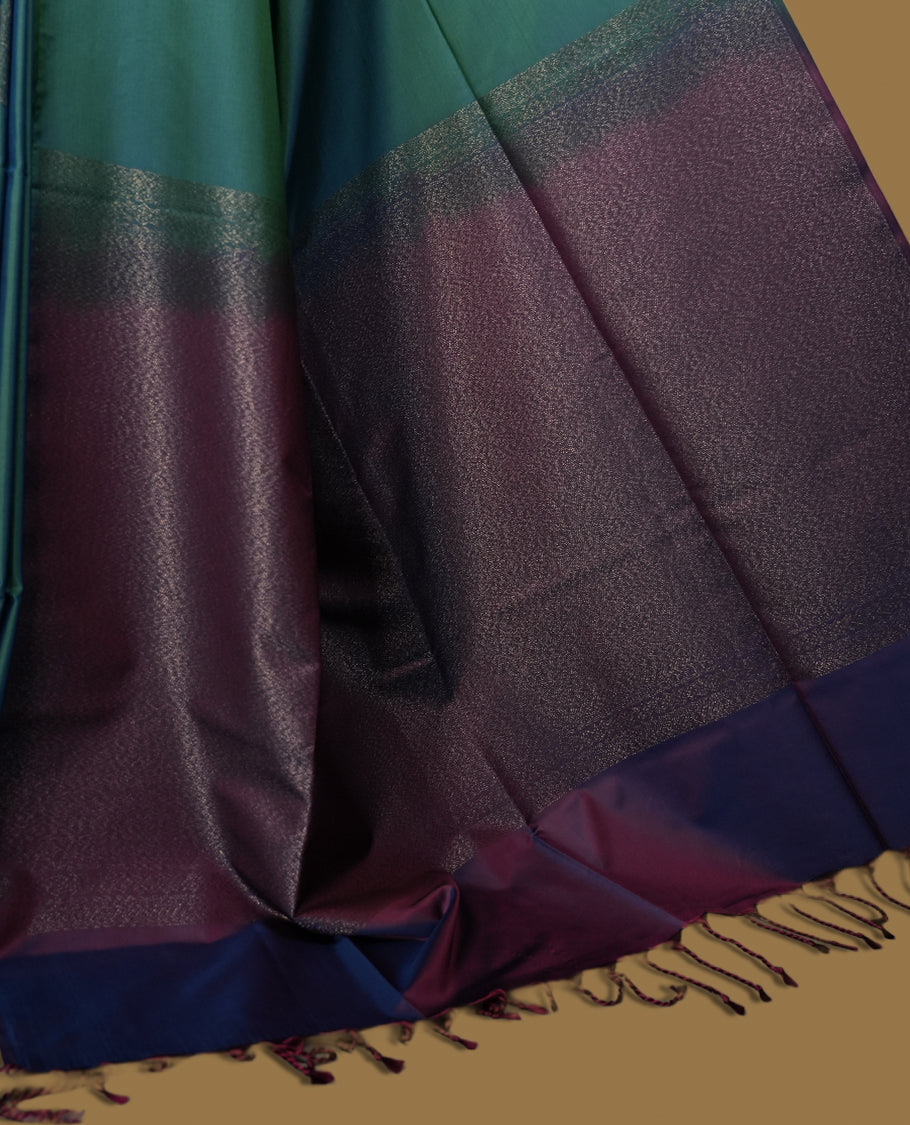 Dual tone blue green semi soft silk saree adorned with woven circular motifs on the body, complemented by a rich contrast plum colour woven pallu with tassel detailing & Comes with a matching blouse piece.