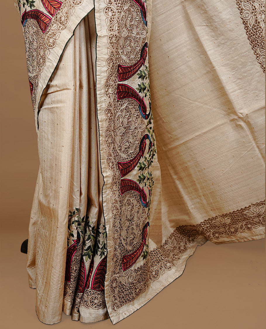 Cream colour Semi Tussar silk saree features an intricate cutwork embroidered peacock motifs on border, paired with a matching unstitched blouse piece.