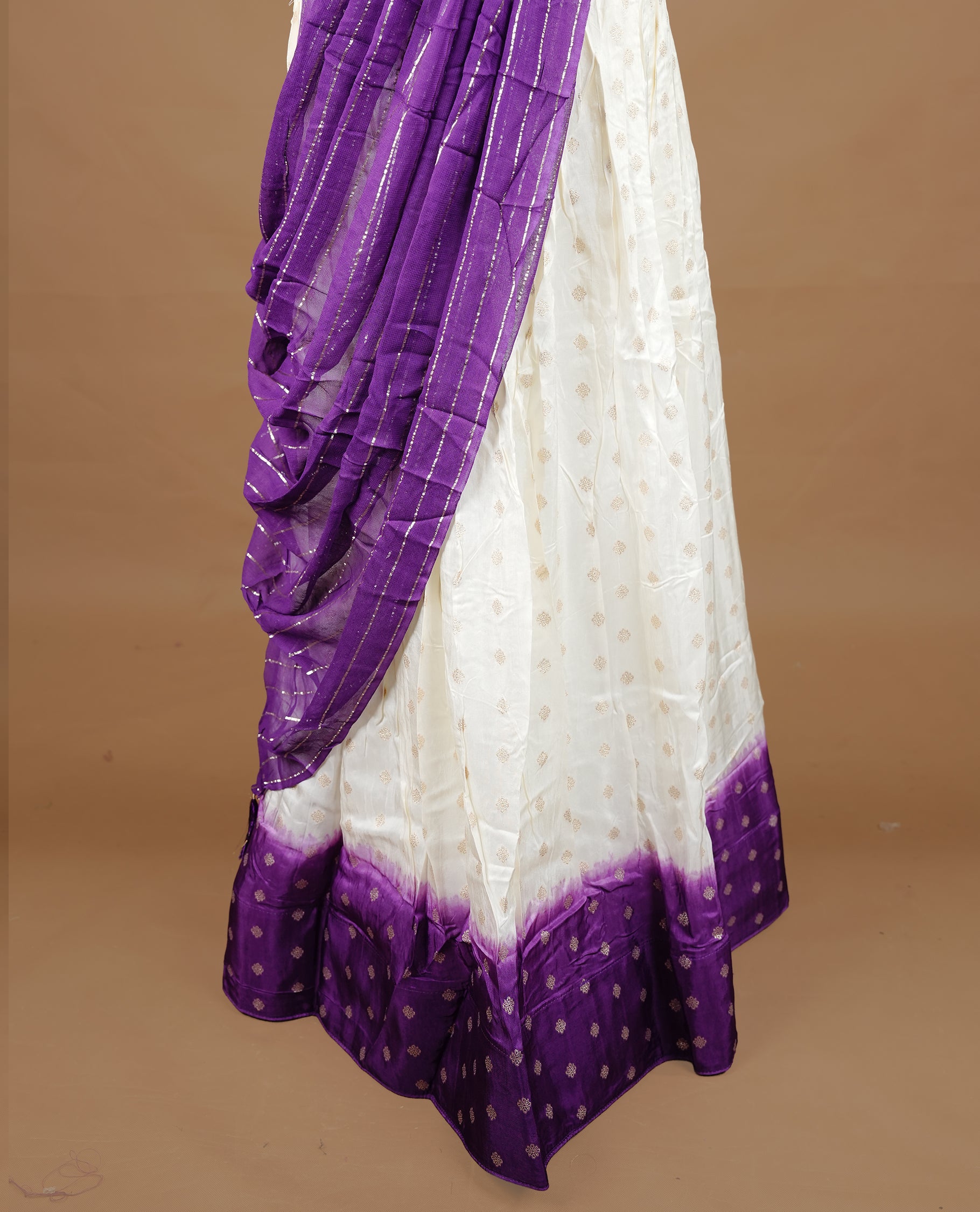 Off white colour semi stitched half saree featuring elegant zari buttas on the body, paired with a contrast purple border and matching striped dupatta,paired with matching blouse piece.
