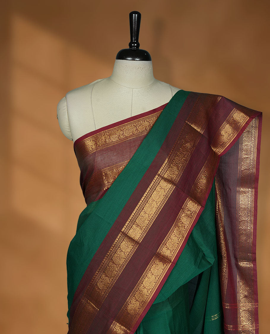 Dark green colour chettinad cotton saree featuring elegant plain body highlighting contrast maroon colour colour with gold zari traditional border, pallu and paired with matching blouse piece.