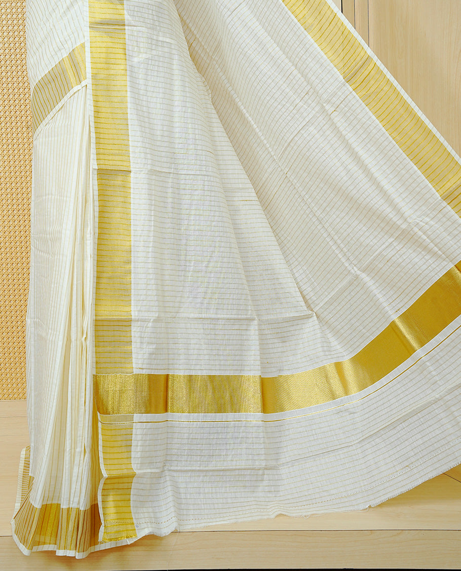 Cream Colur Cotton Kerala Saree Featuring Gold Zari Strips Across On The Body, Classic Gold Zari Border & Pallu,Paired With A Matching Blouse Piece.