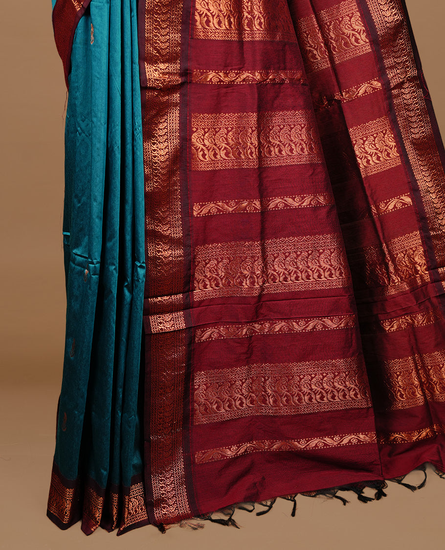 Teal green colour kalyani cotton saree featuring gold zari motifs on body, highlighting contrast Maroon colour with Antique gold zari border, paired with matching blouse piece.
