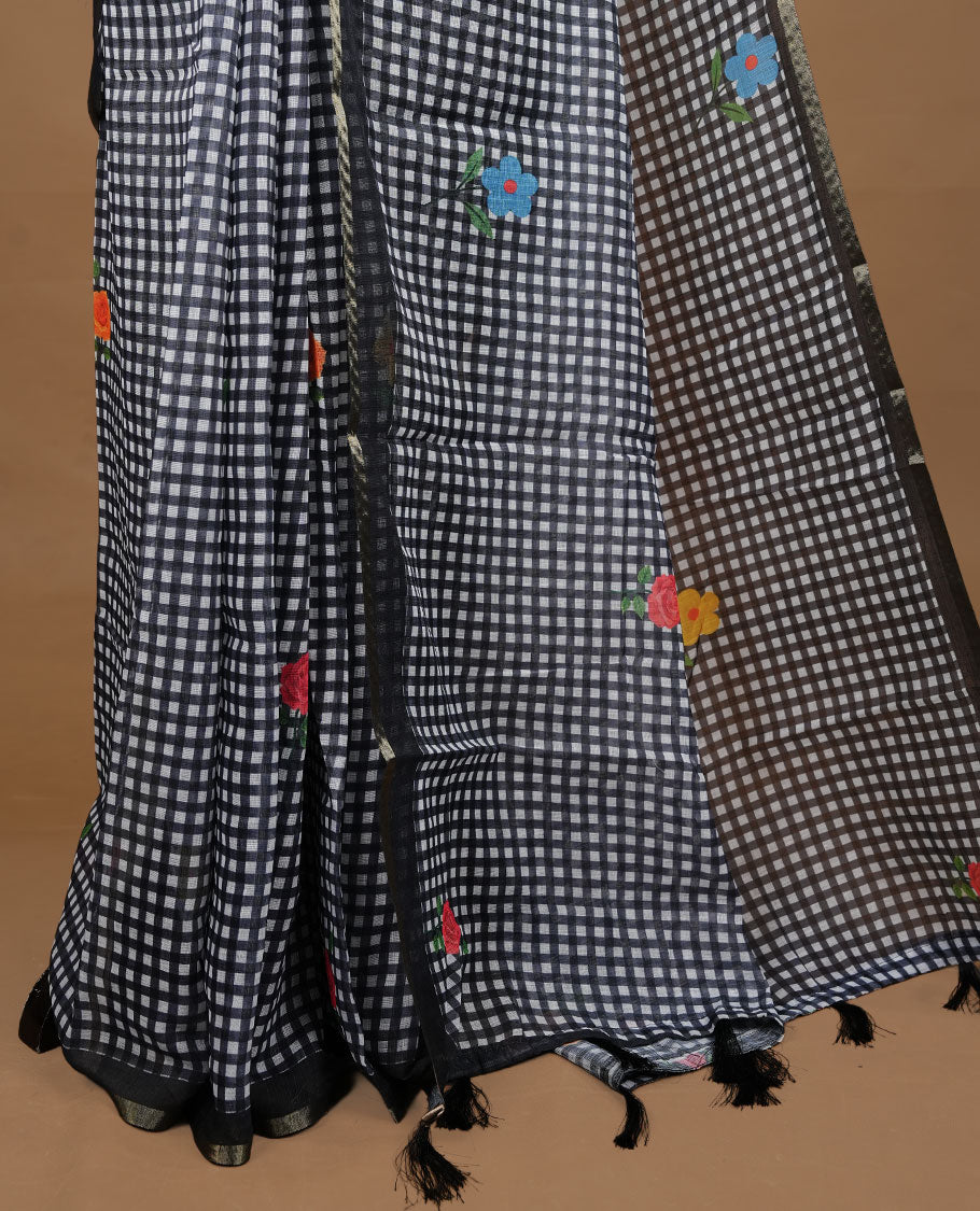 Black colour Semi Linen saree featuring a stylish check pattern adorned with floral prints on the body, enhanced by a small gold border, paired with a matching blouse piece.