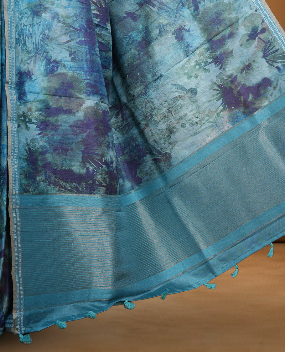 Teal blue colour semi tussar silk saree featuring an abstract floral printed body with a rich self border and tasselled pallu, paired with a matching blouse.