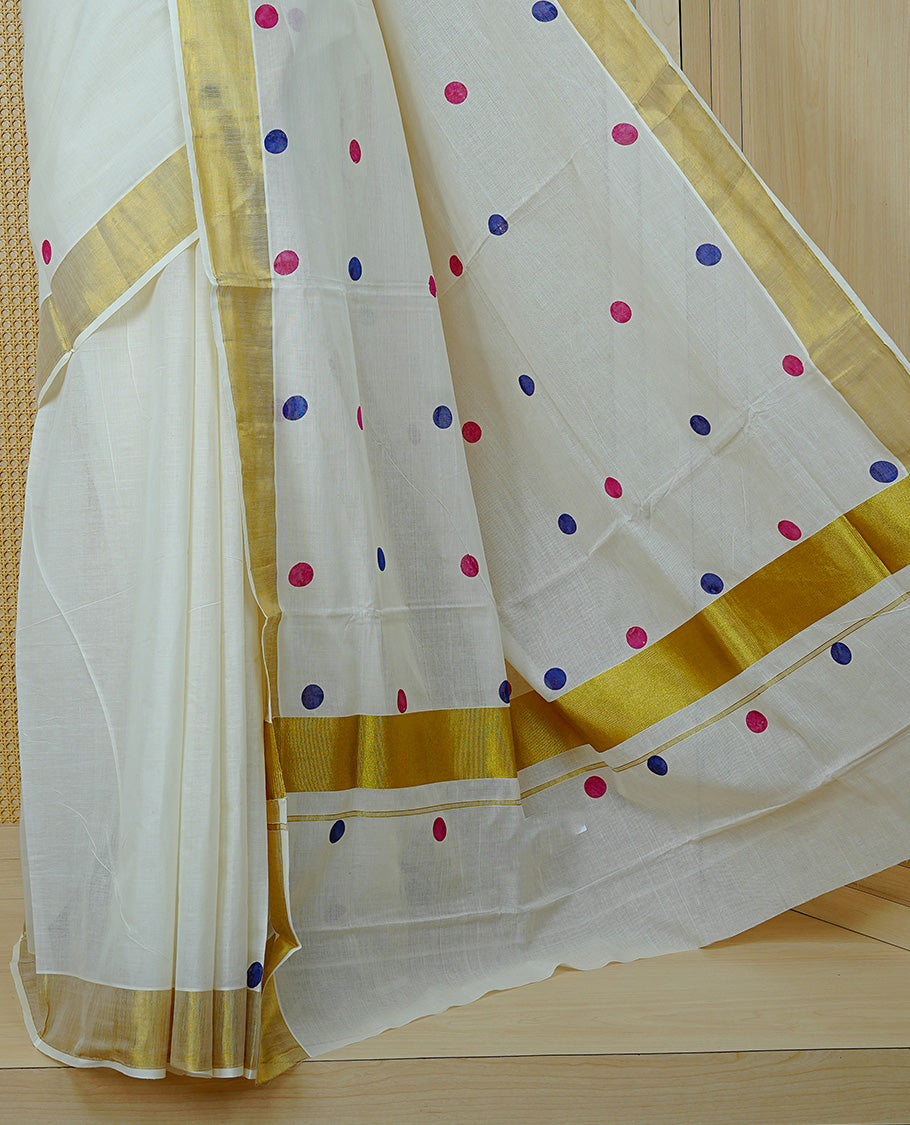 Cream Colour cotton Kerala Saree Featuring Magenta & Blue Dot Prints On The Body, Complemented By A Traditional Gold Zari Border, Paired With A Matching Blouse Piece.