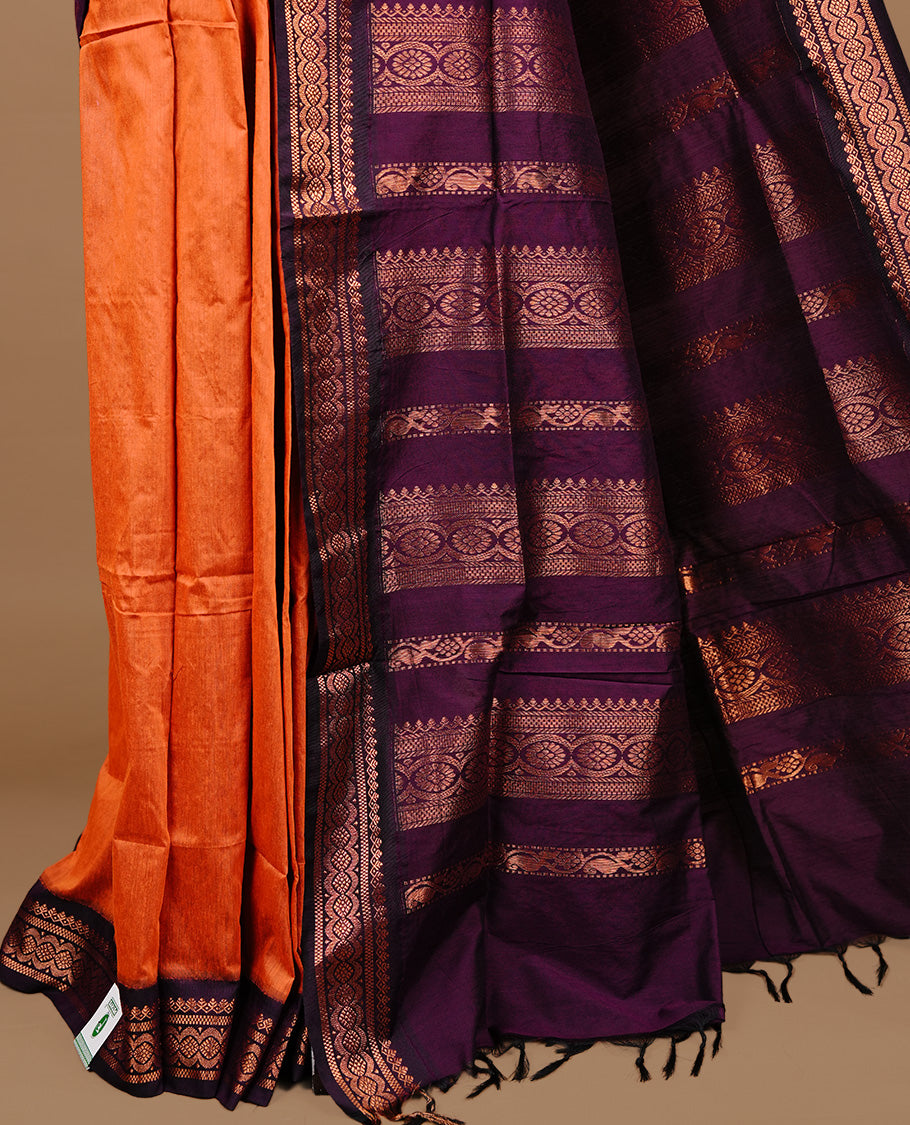 Orange colour kalyani cotton saree featuring gold zari motifs on body, highlighting contrast Purple colour with Antique gold zari border, paired with matching blouse piece.