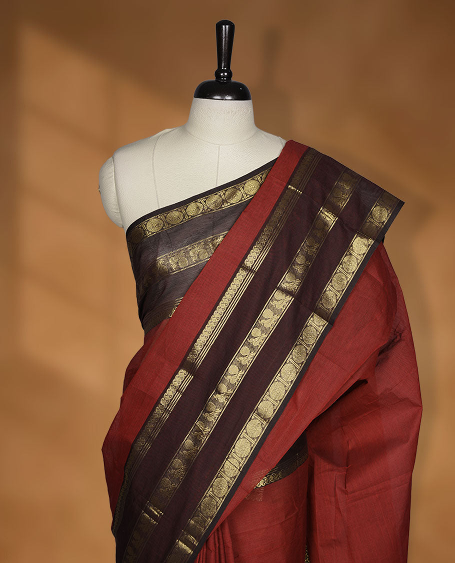 Red colour chettinad cotton saree featuring plain body, contrast chocolate brown colour with traditional gold zari border paired with matching blouse.