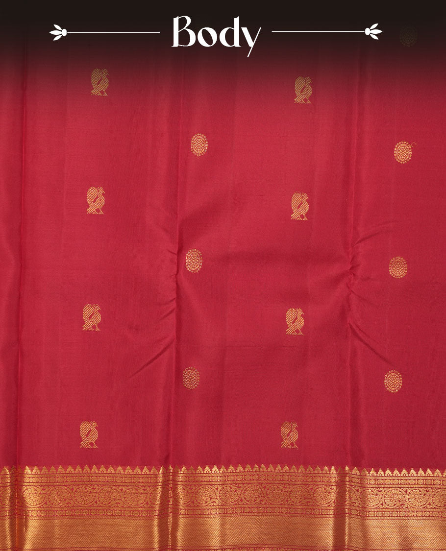 Dark red colour pure traditional Kancheepuram silk saree adorned with elegant zari peacock and chakra motifs on the body, complemented by a simple Gold Zari zari woven border, paired with a matching blouse piece.