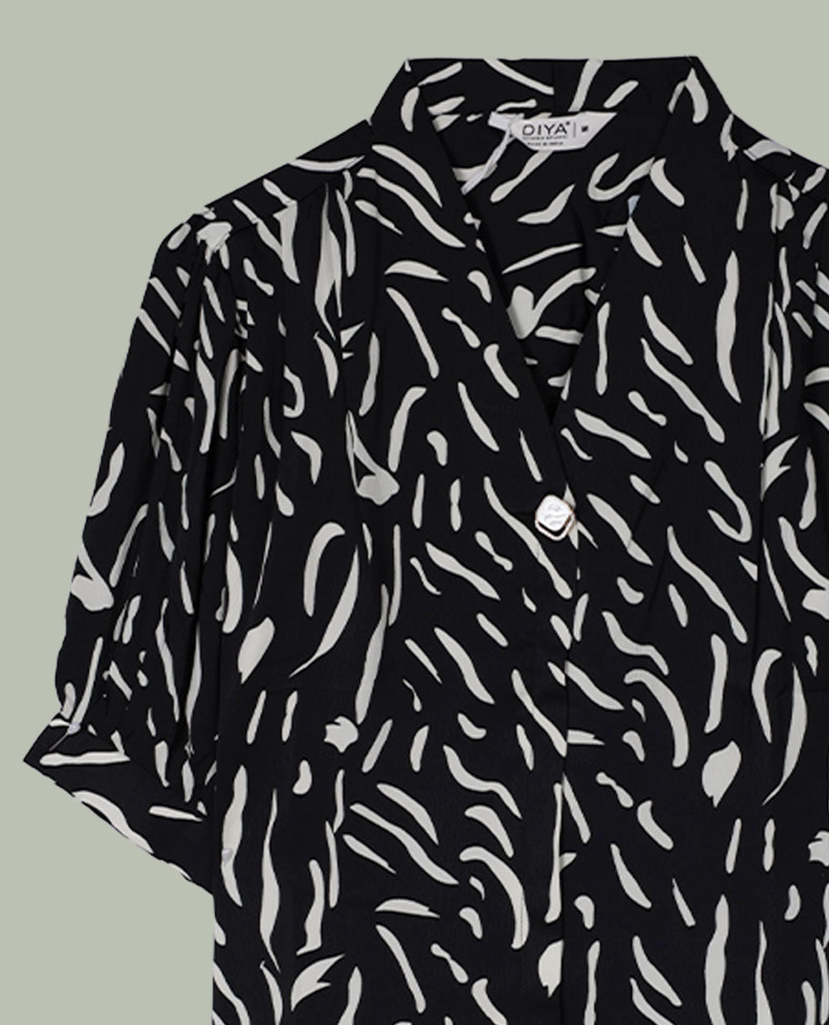 Black short-sleeve shirt top with collared neckline and all-over white abstract dash print, shown from the back.