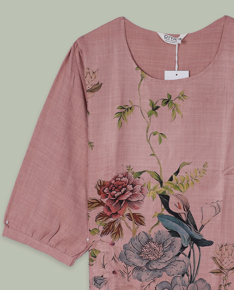 Dusty rose round-neck top with three-quarter sleeves and placement floral print in muted blue, green, and burgundy tones along the front hem and side.