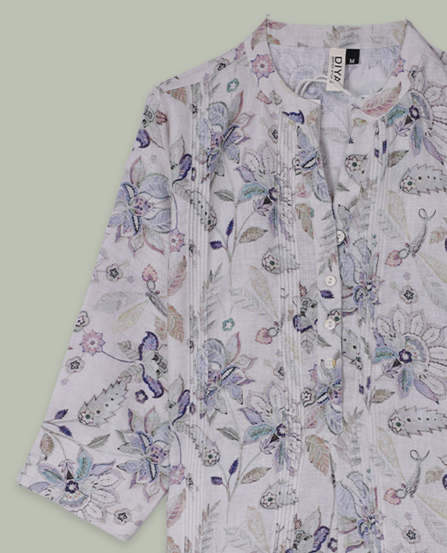 White tunic top with pastel floral and paisley print, band collar, pintuck-detailed front with half button placket, and three-quarter sleeves.