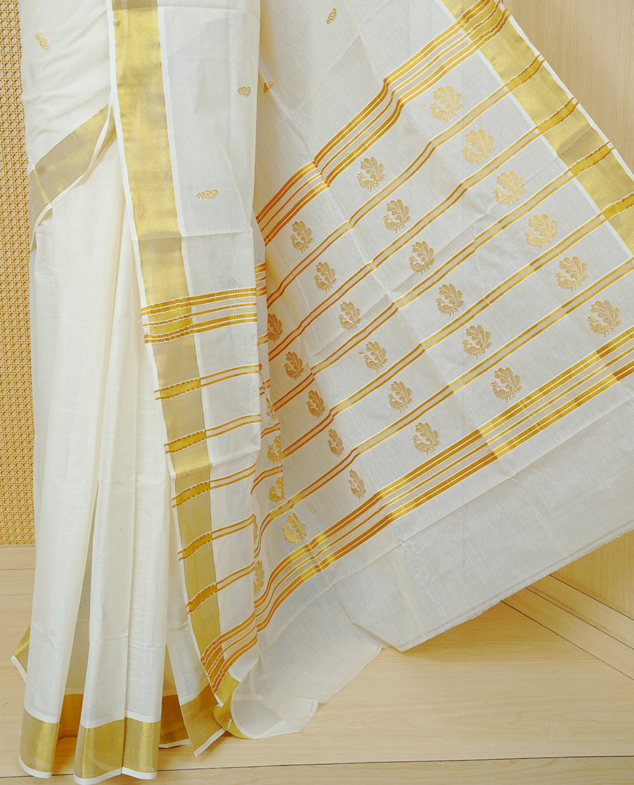 Cream Colour Cotton Kerala Saree Featuring Delicate Gold Leaf Pattern Across The Body, Enhanced With A Traditional Gold Zari Border, A Gold Peacock Motifs & Striped Gold Zari Pallu, Finished With A Matching Blouse Piece