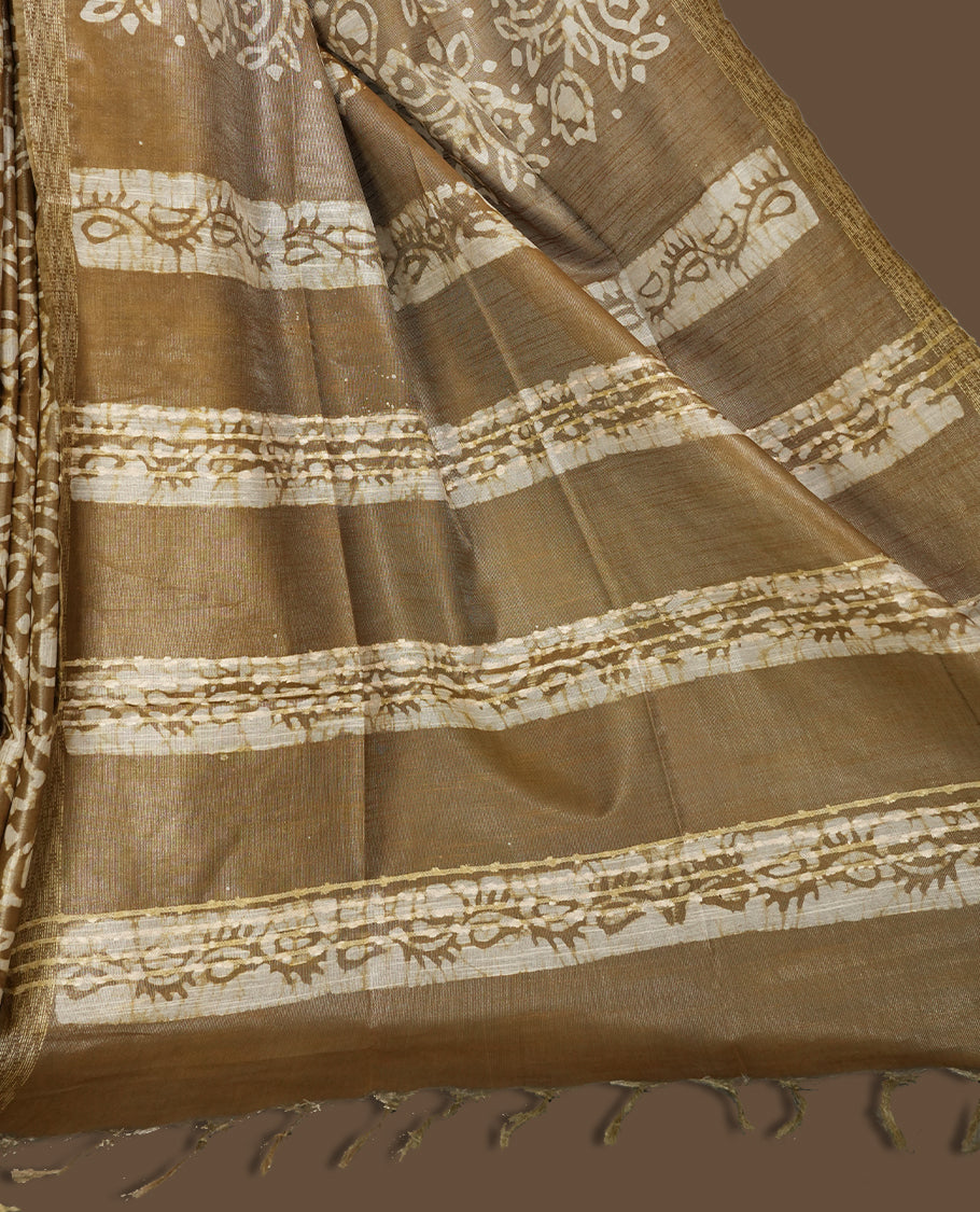 Golden brown semi jute tissue saree featuring elegant floral motifs all over the body, complemented by a shimmering zari striped pallu, woven golden border, and matching blouse piece for a graceful look.