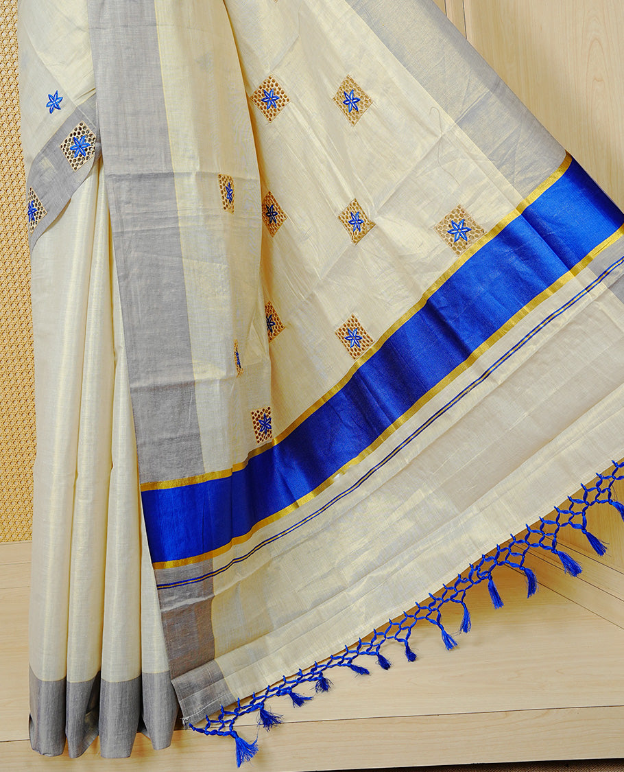 Cream Colour Tissue Kerala Saree Featuring Delicate Blue Floral Embroidery Work Across The Body, Enhanced With A Light Blue Zari Border And A Rich Blue & Gold Zari Pallu, Finished With Blue Tassels And A Matching Blouse Piece