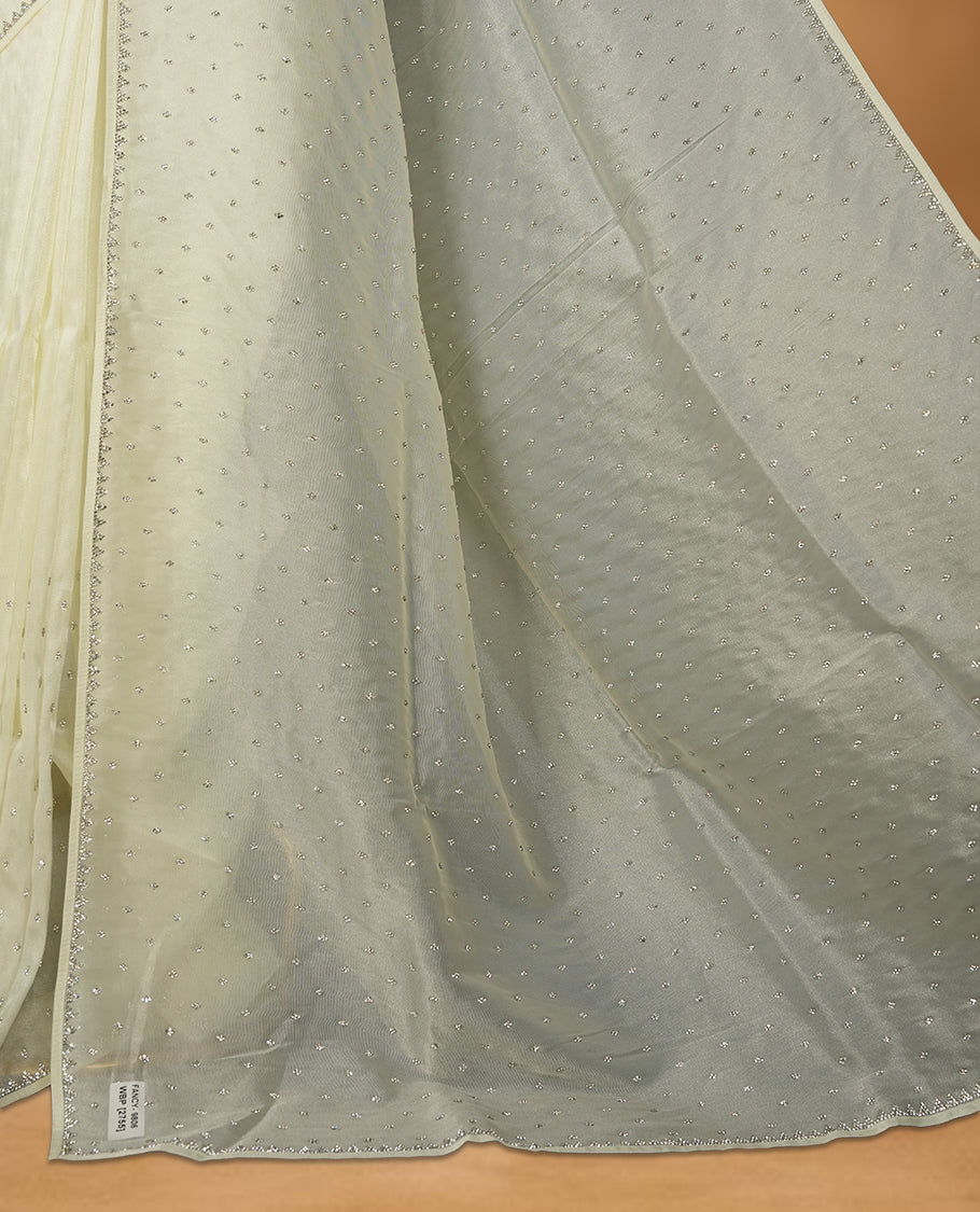 Cream Colour net shimmer fancy saree adorned with white stone buttas all over the body, paired with a delicate stone worked border and matching blouse