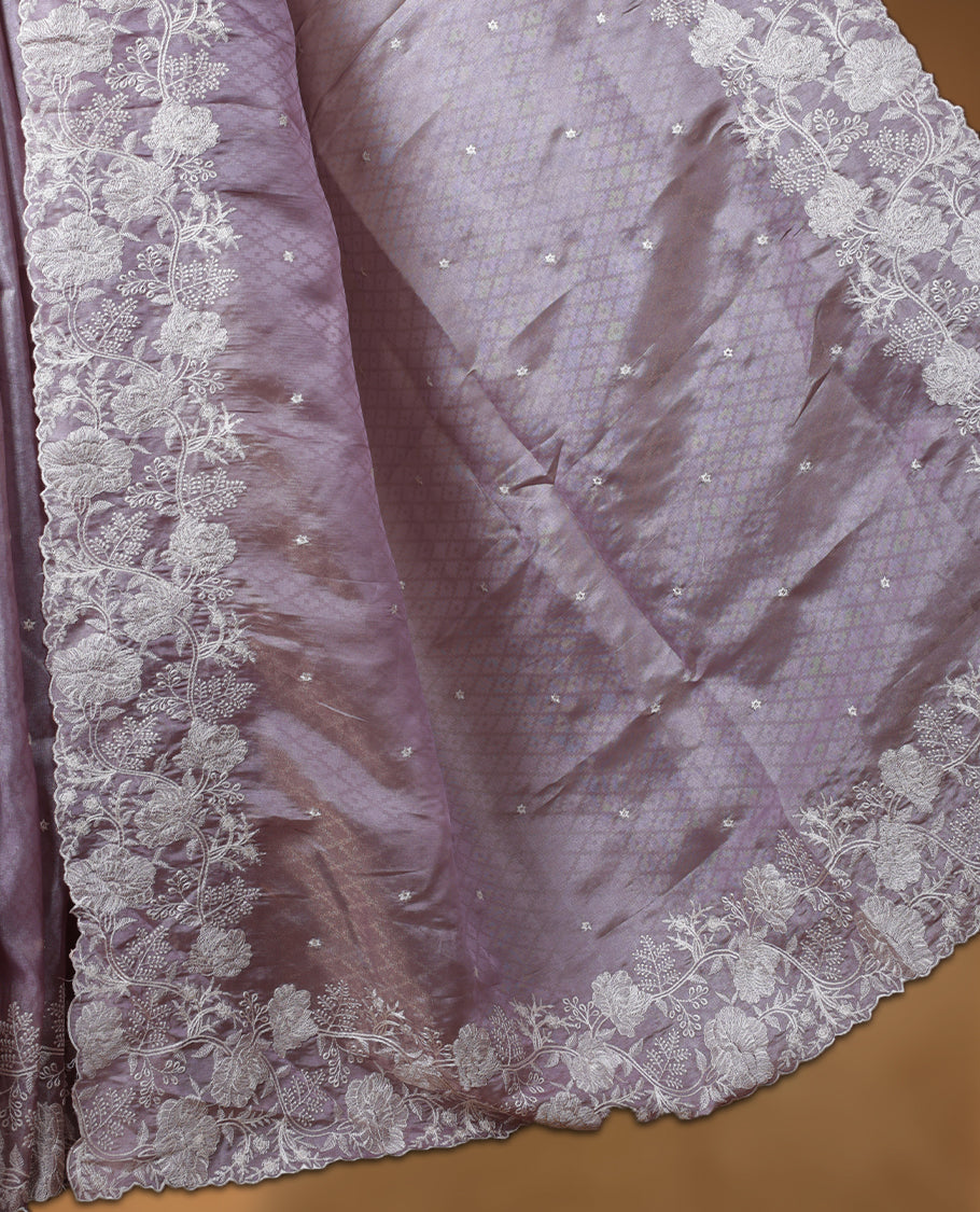 Lavender colour organza designer saree featuring a subtle self patterned body and an intricately scalloped floral thread embroidered border all around, complemented by a coordinating embroidered pallu and paired with a matching blouse.