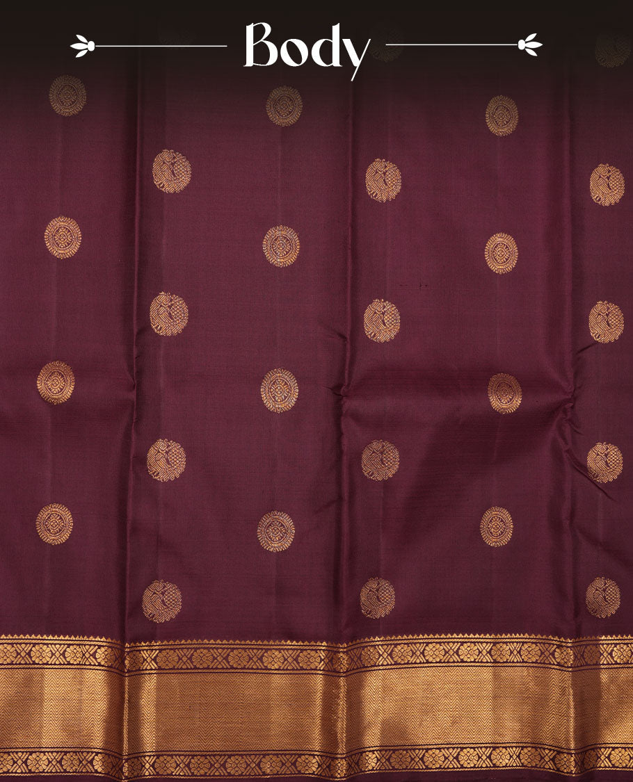 Dark chocolate colour pure traditional Kancheepuram silk saree adorned with elegant peacock and chakra motifs across the body, featuring rich gold zari traditional borders, beautifully paired with a matching blouse piece.