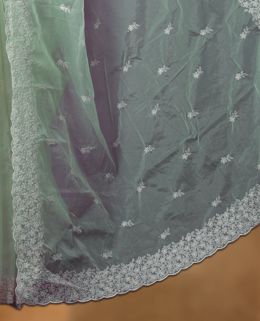 Pastel green colour organza designer saree featuring a subtle self patterned body and an intricately scalloped floral thread embroidered border all around, complemented by a coordinating embroidered pallu and paired with a matching blouse.