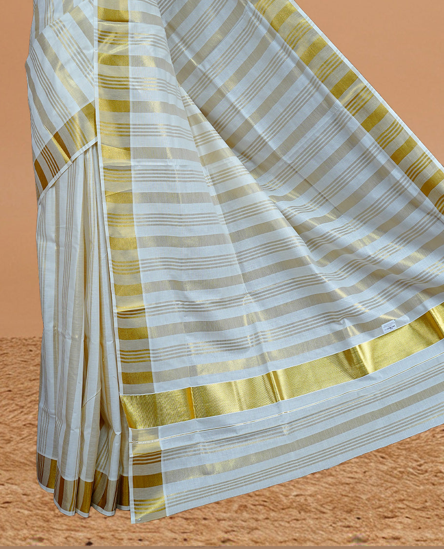 Cream Colour Cotton Kerala Saree Featuring Gold zari stripes On The Body & Classy Gold zari border, Paired With A Matching Blouse Piece.