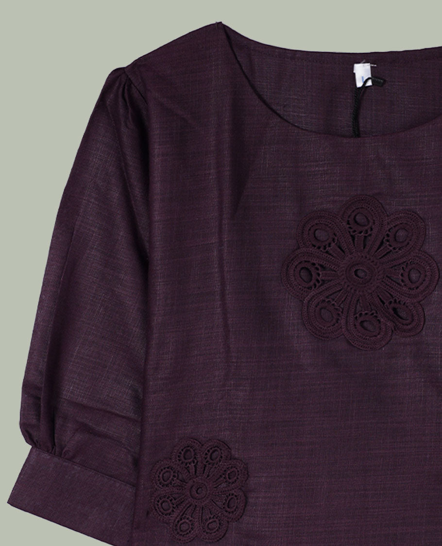 Deep plum three-quarter sleeve top with round neckline and tonal crochet floral appliqués placed at the center front and near the hem