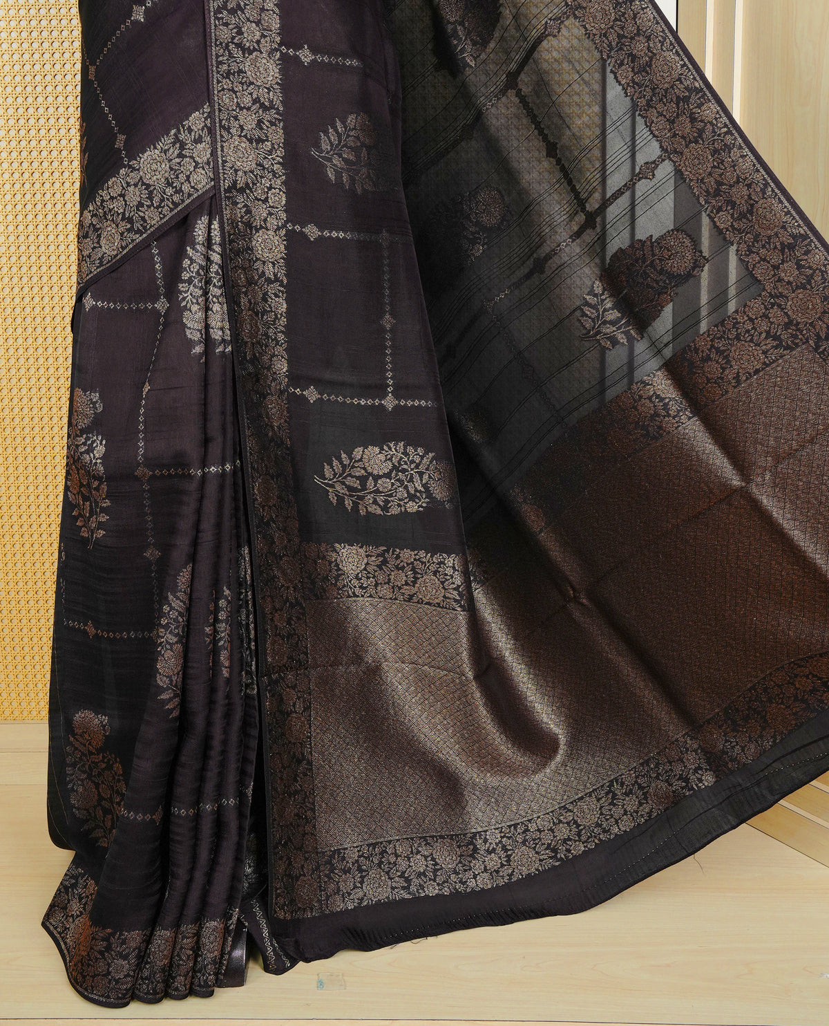 Black colour semi banaras tussar georgette saree featuring gold zari floral pattern on body, finished with gold zari floral motifs on border and paired with matching blouse piece.