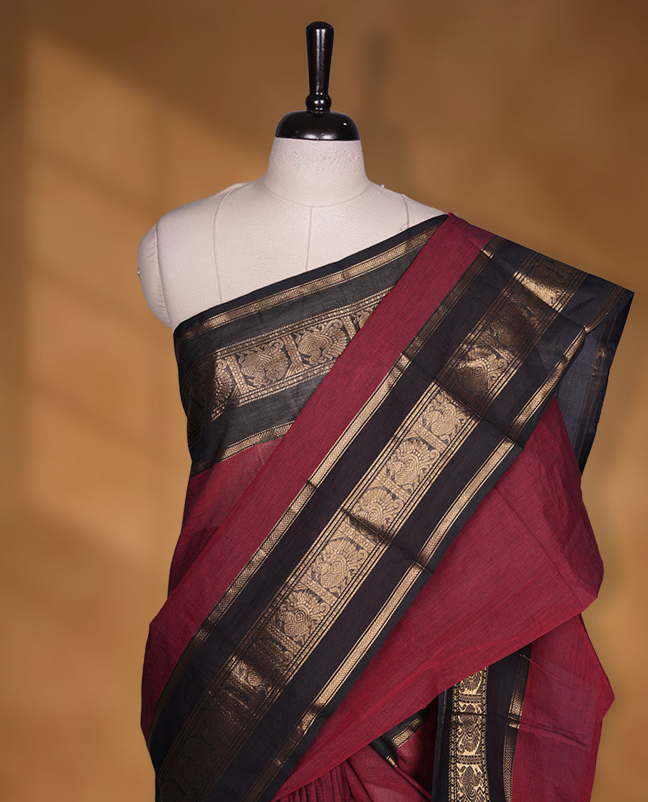 Dark red colour chettinad cotton saree featuring plain body, paired with a black colour traditional gold zari border paired with matching blouse.