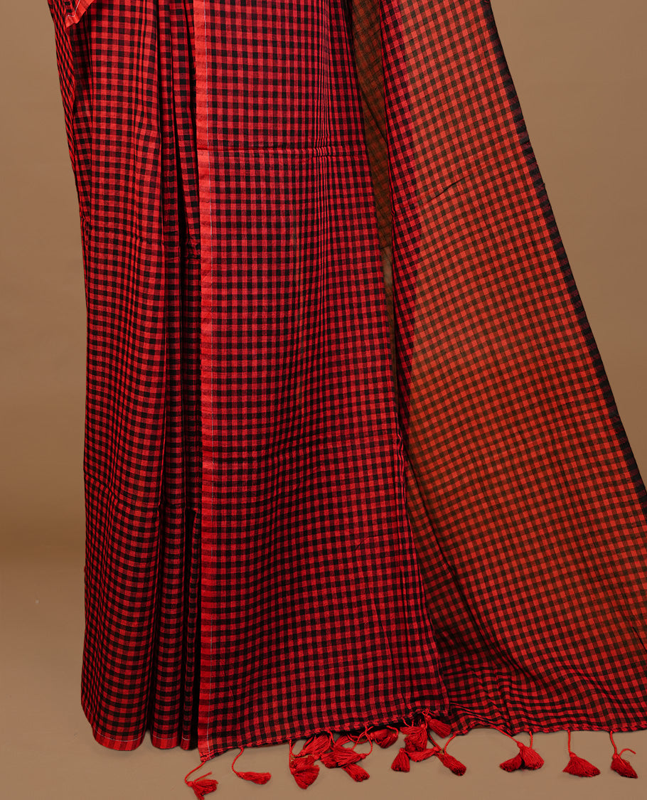 Red and Black colour Mul Cotton saree featuring a classic small check pattern on the body, accented with tassels for added charm. Comes without a blouse piece.