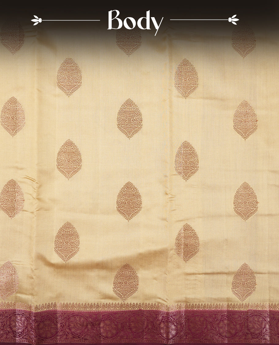Cream Colour Banaras Soft Silk Saree with Gold Zari Oval Leaf Buttas, Intricate Multi-Layered Floral Border, Grand Pallu with Intricate Brocade Motifs in Deep Maroon and Gold Tones, and Matching Blouse.
