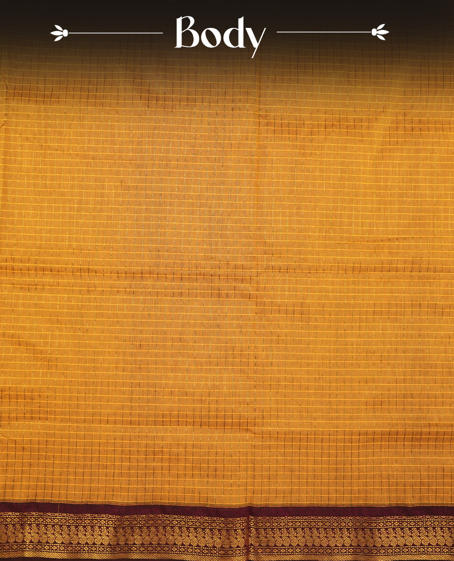 Mustard yellow coloured mixed Kalyani cotton saree featuring golden zari checks on the body, complemented by a grape purple coloured border and pallu adorned with golden zari patterns, Paired with a matching blouse.