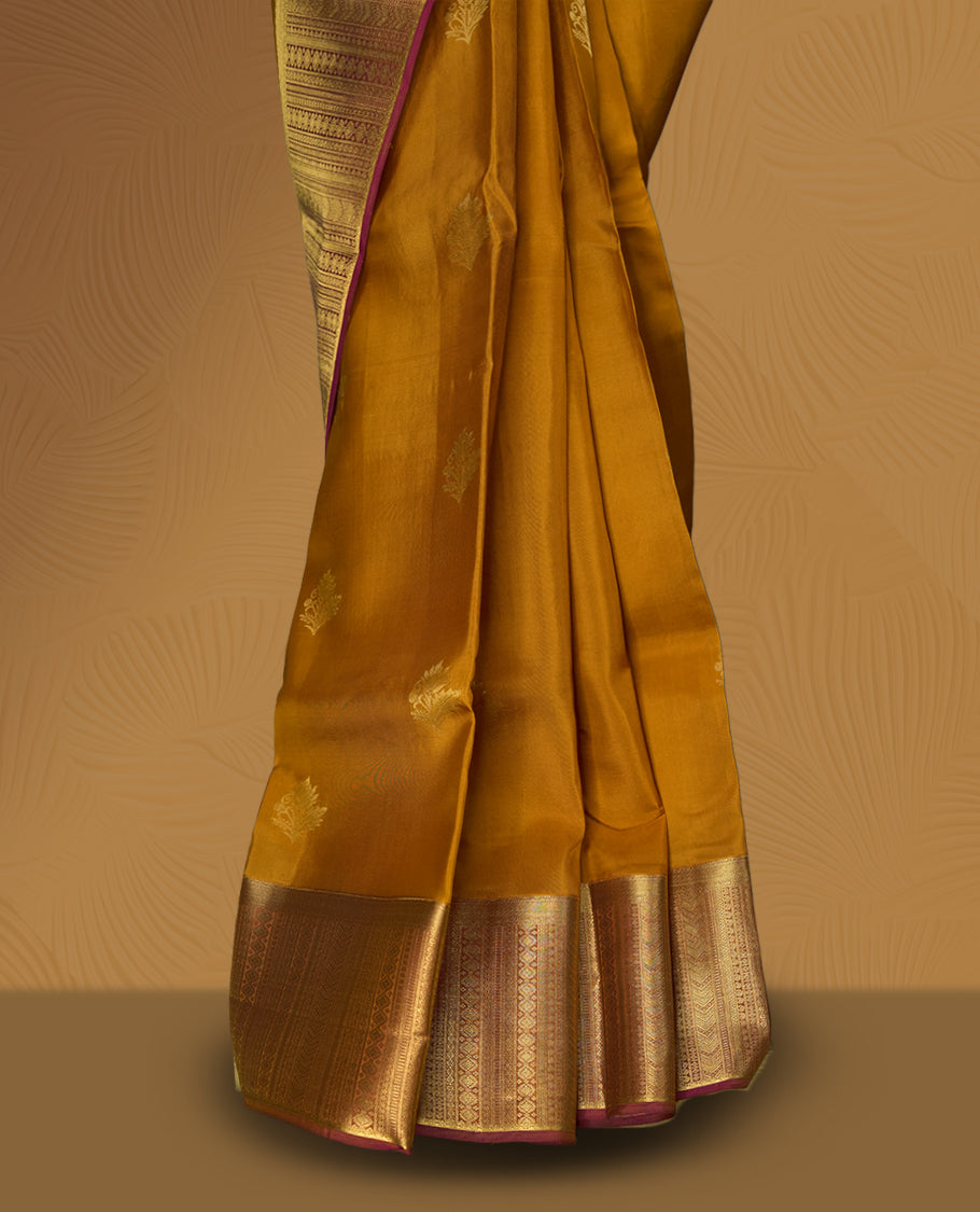 Ochre yellow colour soft silk saree adorned with small golden buttas, enhanced by a rich gold zari border and pallu with intricate detailing & paired with a matching blouse.