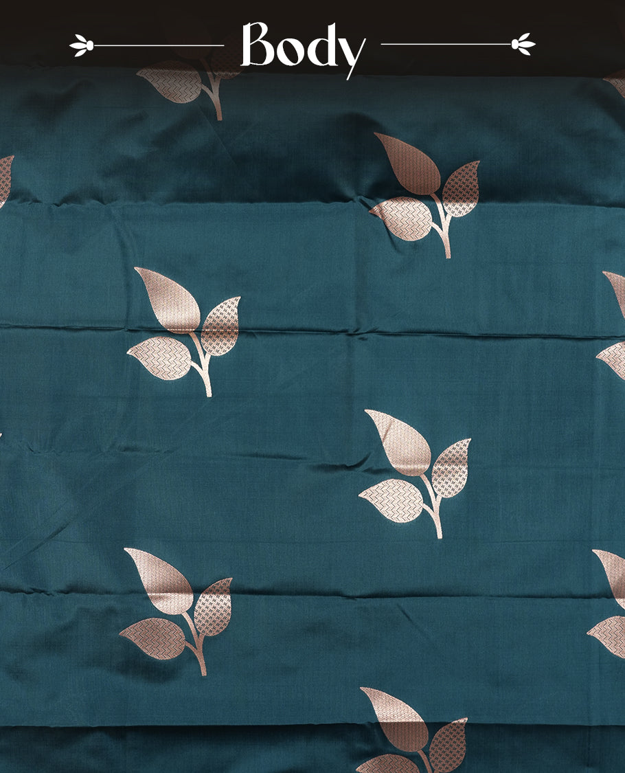 Dark teal blue colour semi silk saree adorned with elegant floral motifs on the body, complemented by a shimmering golden zari-woven pallu and border, and paired with a matching blouse