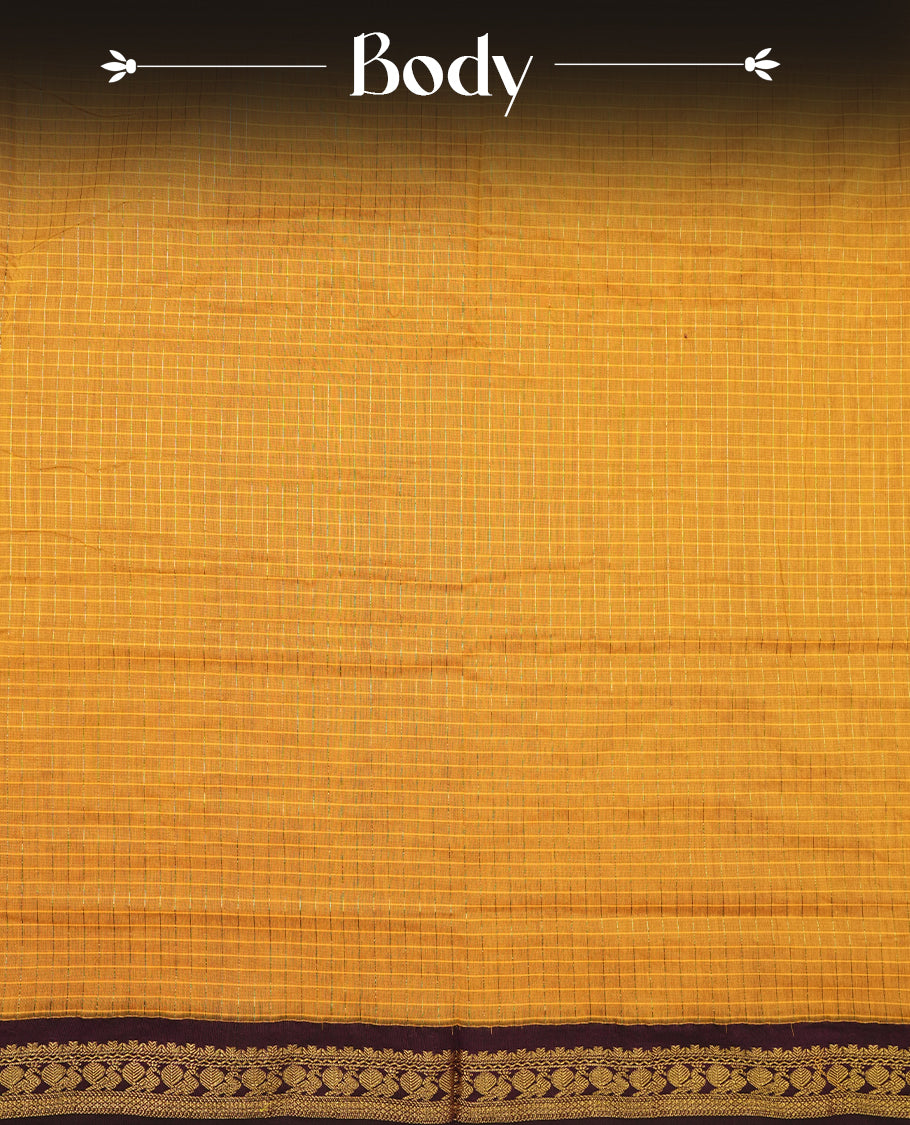 Mustard Yellow coloured mixed Kalyani cotton saree featuring golden zari checks on the body, complemented by a dark purple coloured border and pallu adorned with golden zari patterns, Paired with a matching blouse.
