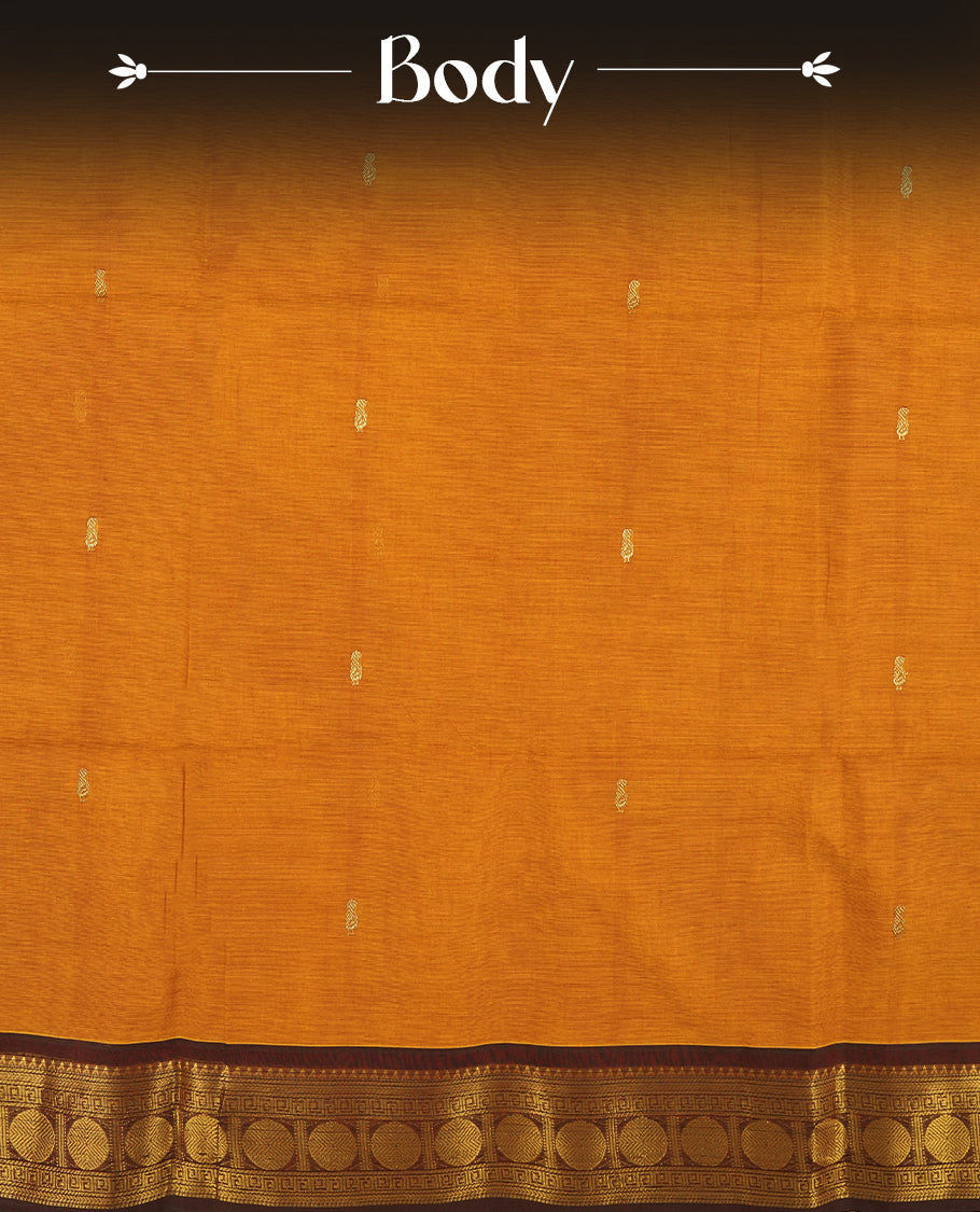 Mustard Orange colour Chettinad cotton saree adorned with small woven motifs on the body, The saree features a deep maroon border highlighted with intricate golden zari circular patterns and comes with a matching blouse piece.
