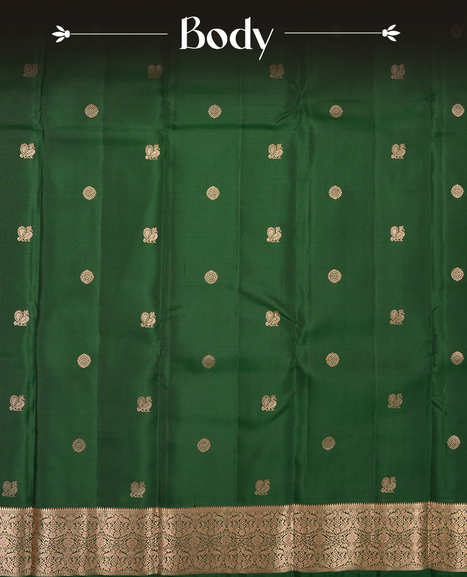 Dark Green colour Vasundhara silk saree adorned with all-over gold chakkaram & mayil motifs on the body, complemented by a gold tarditional border and paired with a matching blouse piece.