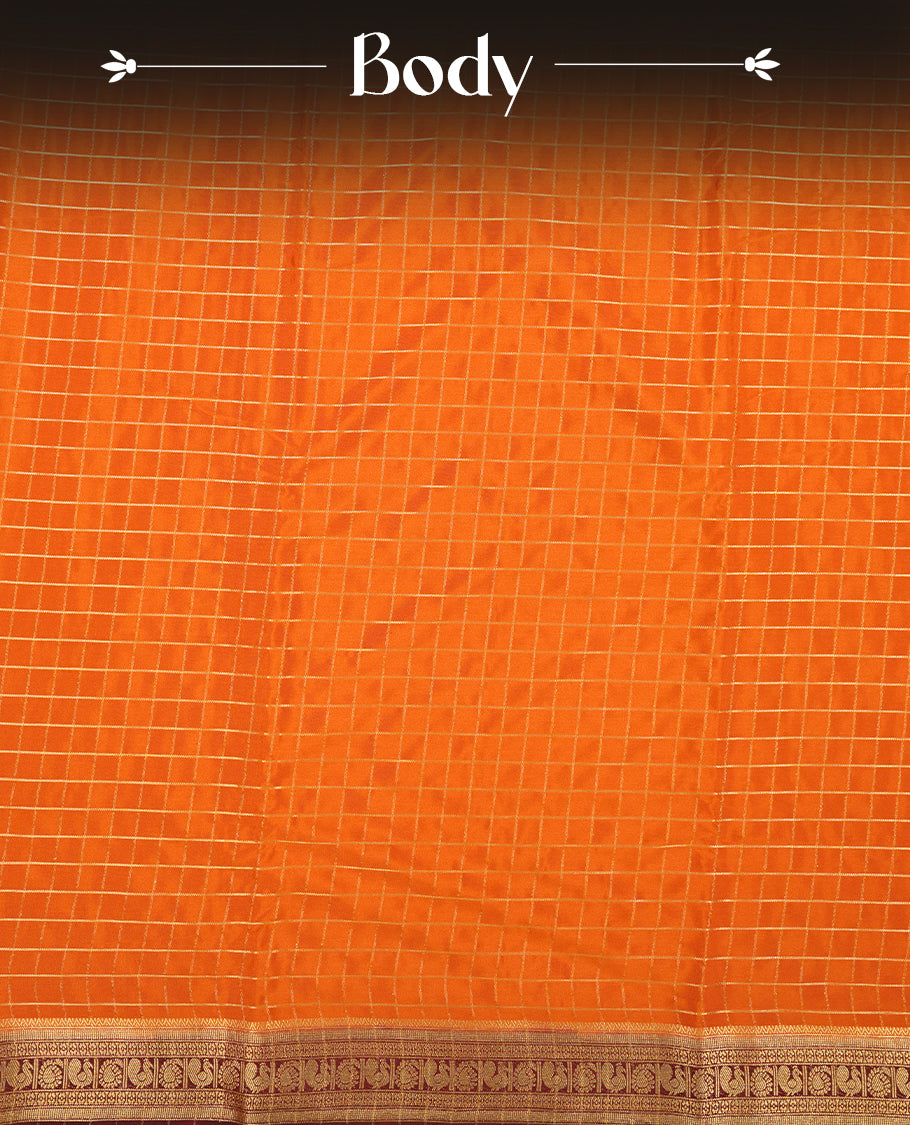 Orange colour mysore crepe saree with gold zari check pattern on body, complemented by contrast Chocolate brown colour border featuring peacock and chakkram motifs, paired with matching blouse.