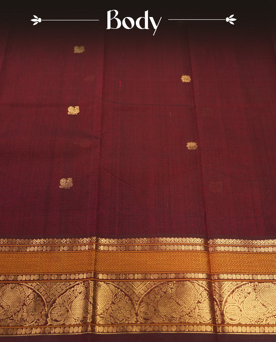 Maroon colour Pure Kanchi cotton saree adorned with subtle golden buttas all over, highlighted by a rich zari woven border with traditional motifs & Includes a matching blouse piece for a complete look.