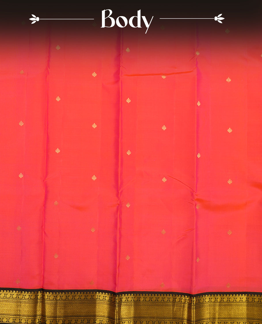 Pinkish red colour Vasundhara silk saree adorned with all-over gold zari motifs on the body, complemented by a contast black colour with gold motifs on border and paired with a matching blouse piece.