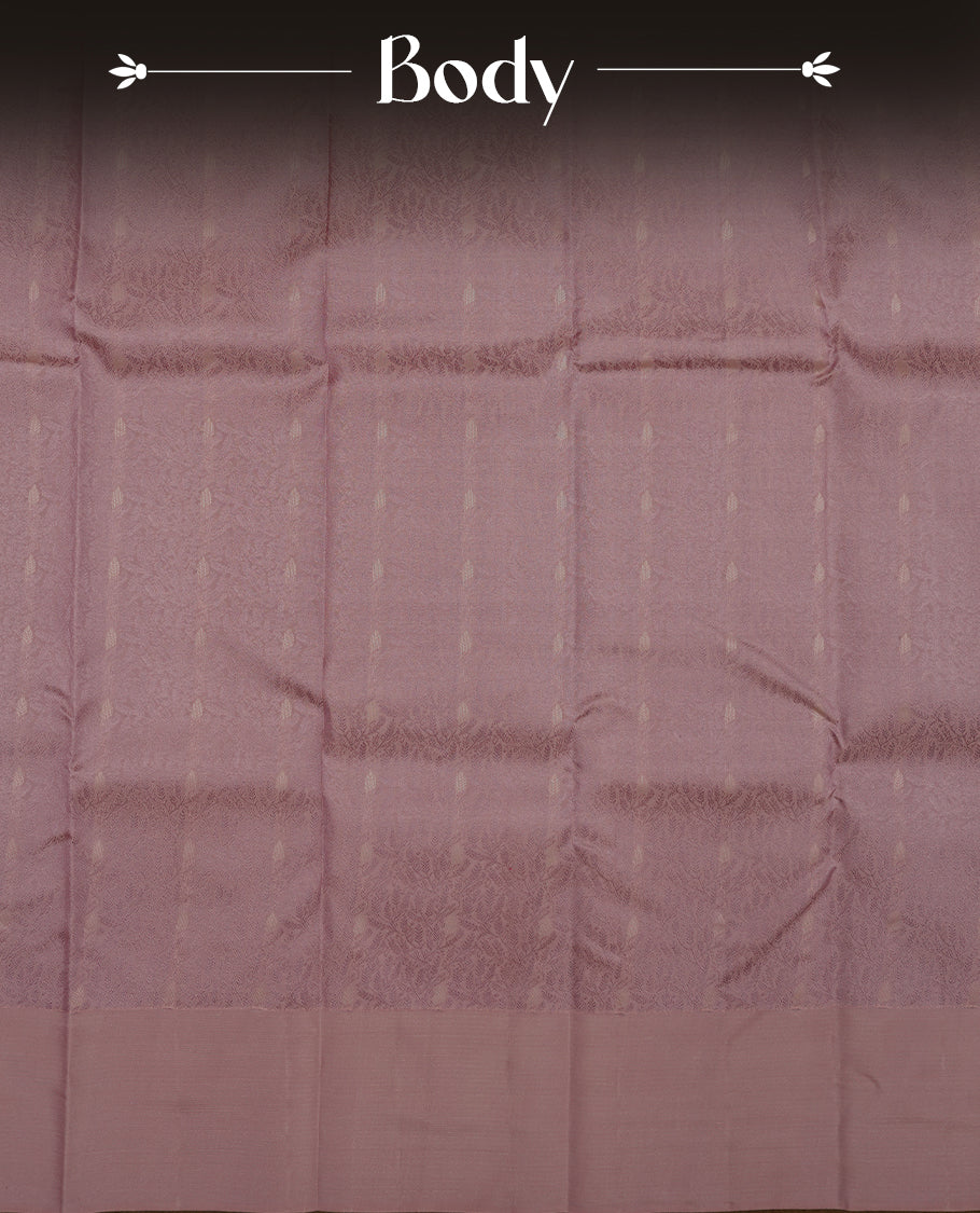 Dusty lavender colour Vasundhara silk saree adorned with all-over self color leaf kodi motifs on the body, complemented by a self colour with gold line pattern border and paired with a matching blouse piece.