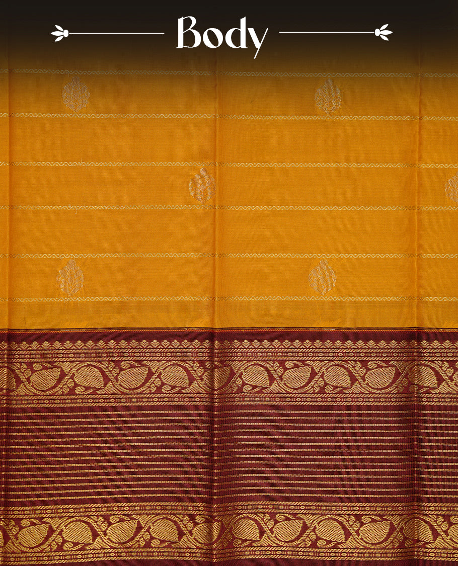 Mustard coloured soft silk saree featuring gold zari stripes and motifs across the body, enhanced with a contrast Maroon border and pallu, paired with a matching contrast blouse piece.