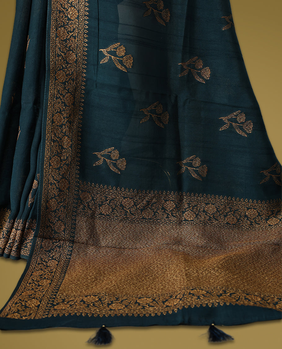 Dark teal green semi Banaras tussar saree adorned with golden floral motifs along the border and scattered designs across the body, finished with a rich golden zari pallu, paired with a matching blouse.