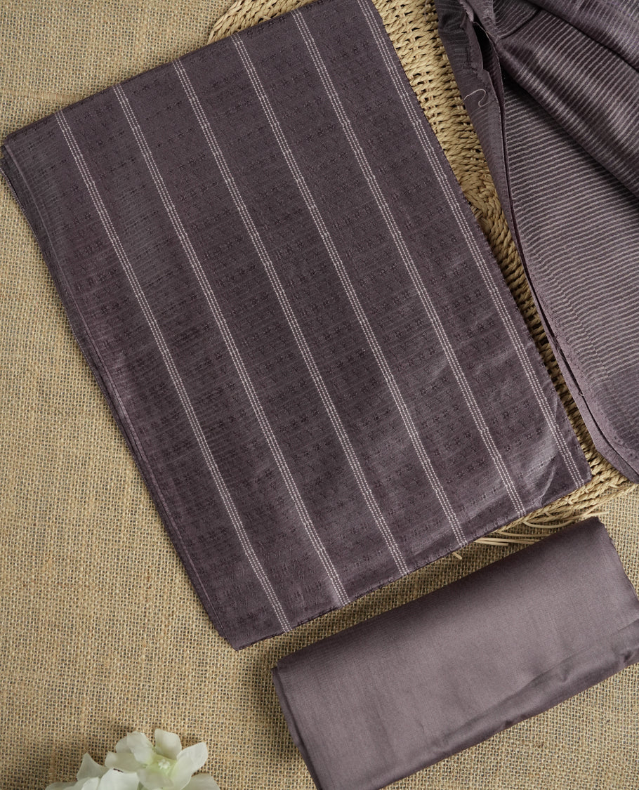 Dark pastel purple colour tussar suit material featuring a subtle self woven pattern and vertical lines on the body, paired with a lightweight matching dupatta with tassel edges and a plain bottom piece.