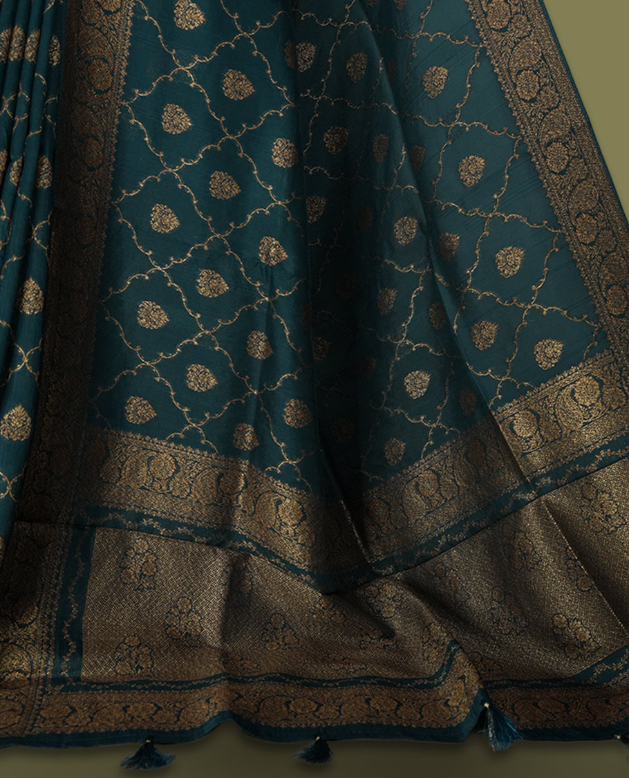 Deep peacock blue colour semi Banarasi Tussar Georgette saree with gold zari motifs on the body, a grand woven golden pallu, and ornate zari border. Includes a matching blouse piece for a complete look.