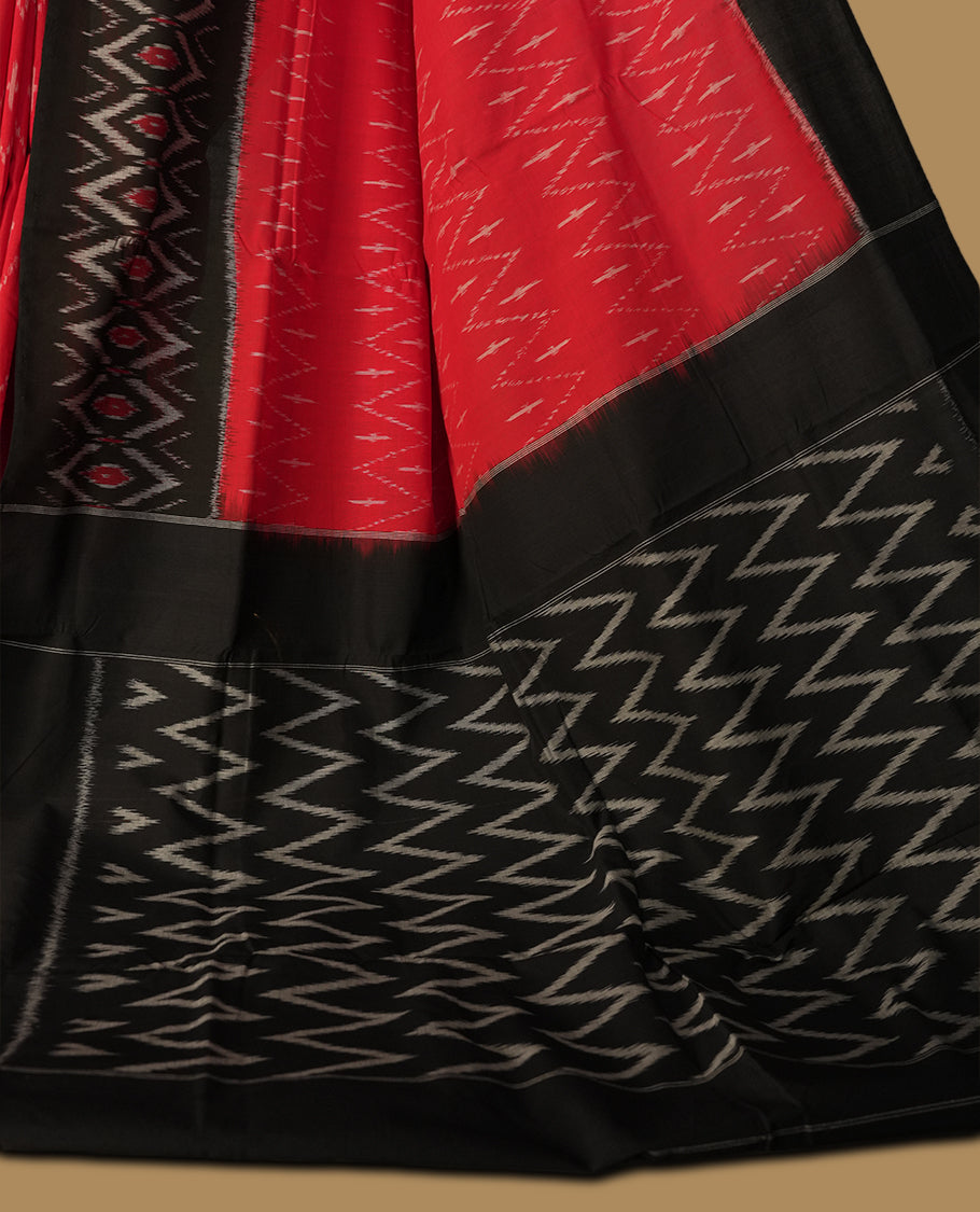 Red colour Ikkat Pochampally saree with bold zigzag motifs and contrasting black borders, The striking woven pallu enhances its elegance, making it a perfect blend of tradition and style.