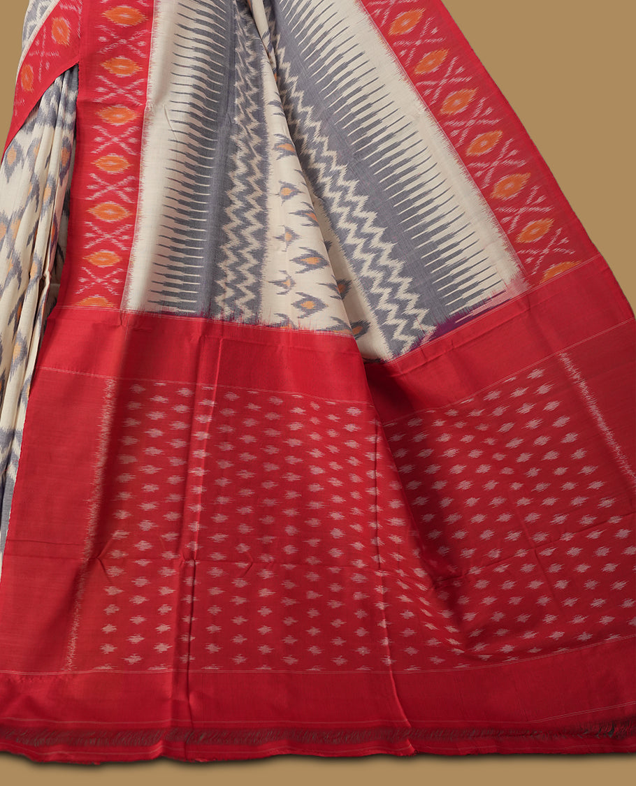 Off white colour Ikkat Pochampally saree adorned with blue & sandy brown geometric patterns, paired with a striking red border and pallu featuring traditional ikat motifs, a timeless blend of vibrance and tradition.