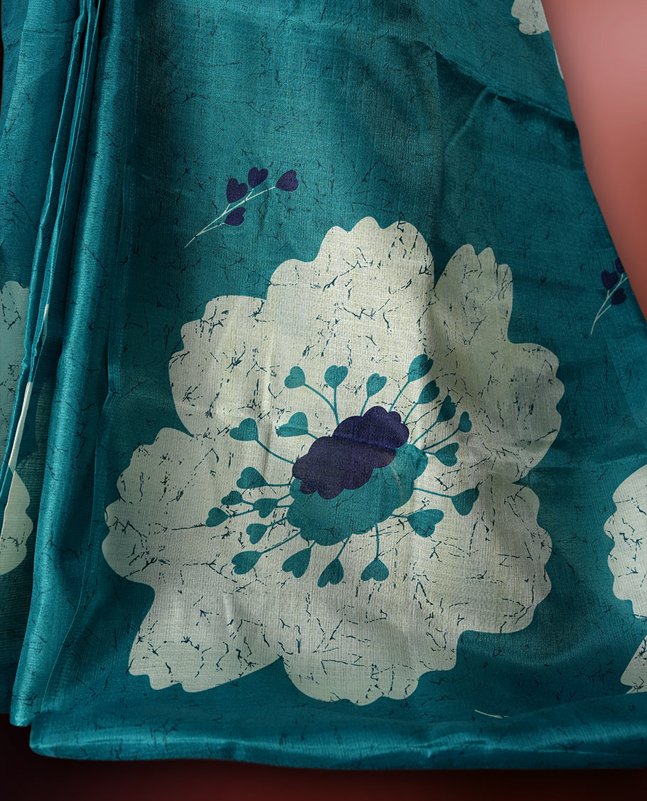 Teal blue colour saree with bold white floral motifs and subtle navy blue accents, exuding timeless elegance and modern charm, paired with a matching blouse.