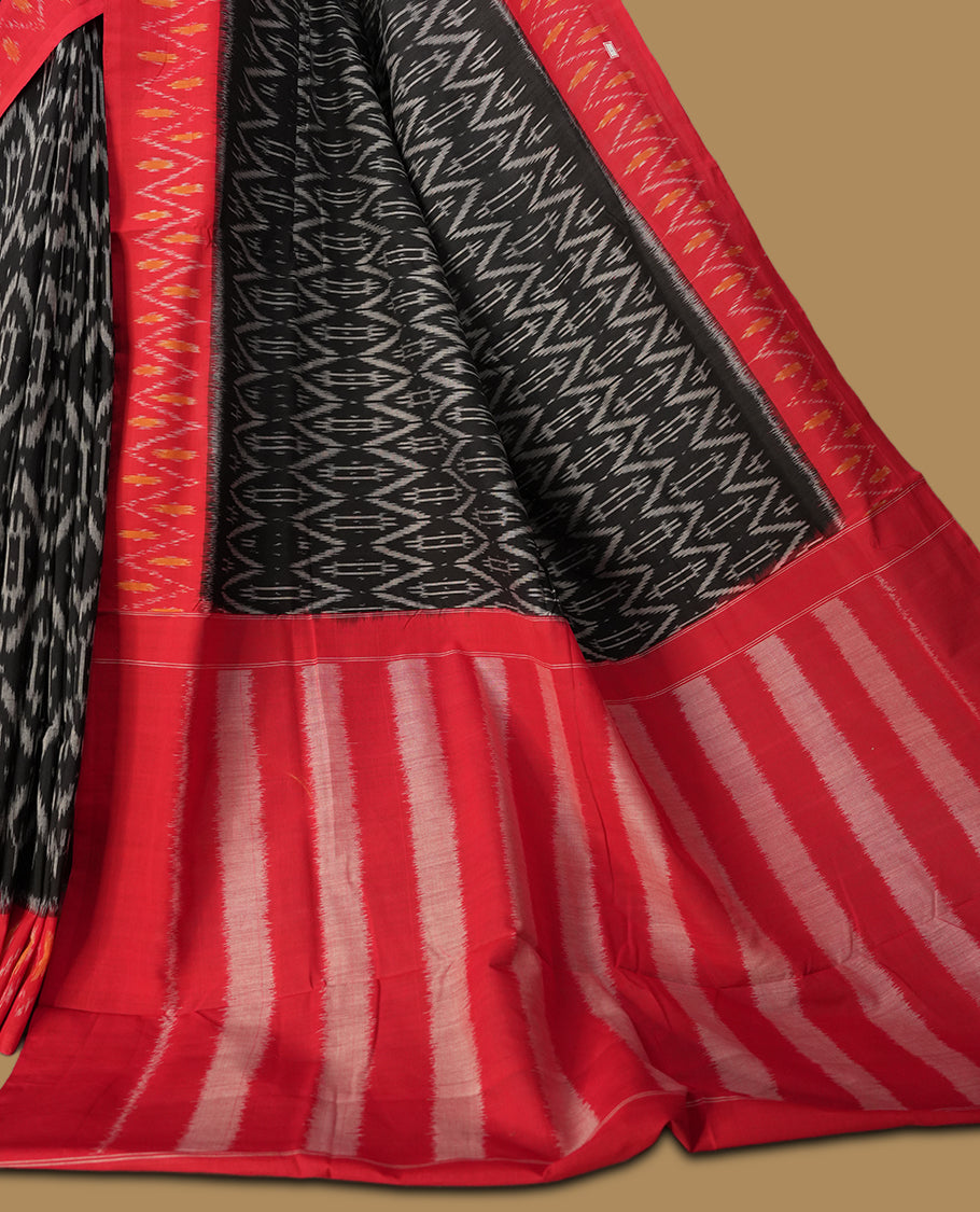 Black colour Ikkat Pochampally saree featuring bold geometric motifs in grey colour with a striking red colour contrast border with grey and orange colour zigzag & beautifully blending tradition with elegance.