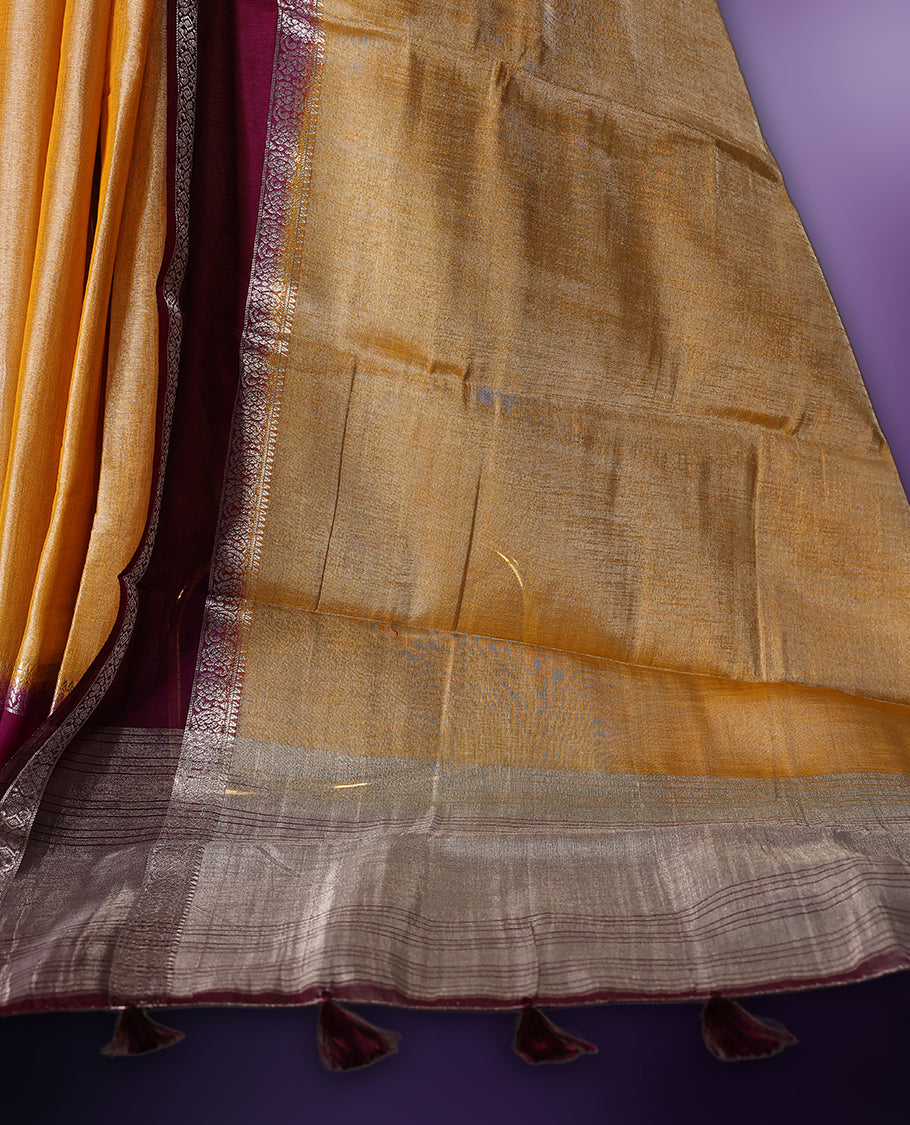 Golden yellow saree with a rich maroon border and pallu, accentuated by delicate silver zari detailing and tassel finish & The fabric has a lustrous sheen and comes with a matching blouse piece.