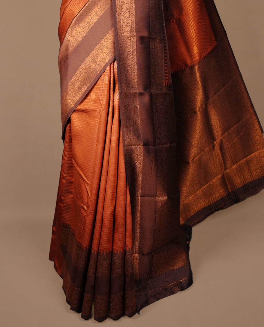 Burnt orange colour silk saree featuring gold zari small square and motifs on body, complemented by contrast chocolate with traditional border, paired with matching blouse piece.