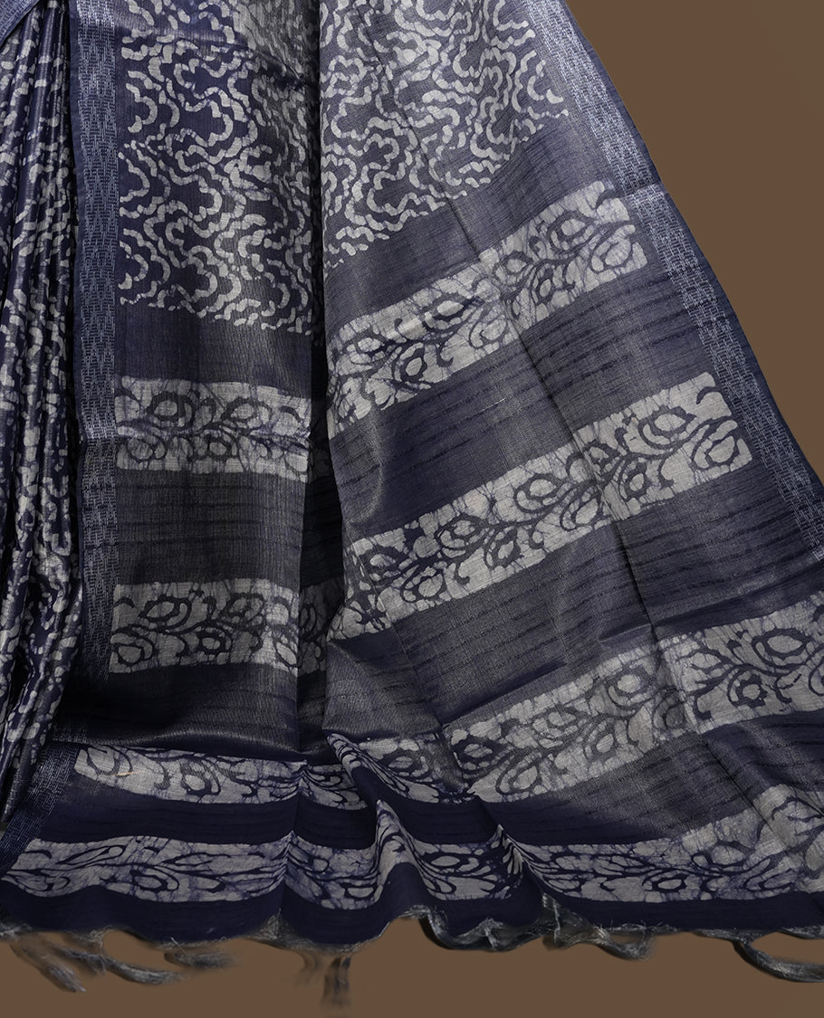 Greyish blue colour semi jute tissue saree featuring white floral prints across the body, adorned with intricate geometric woven borders and a graceful floral work pallu & Comes with a matching blouse piece.